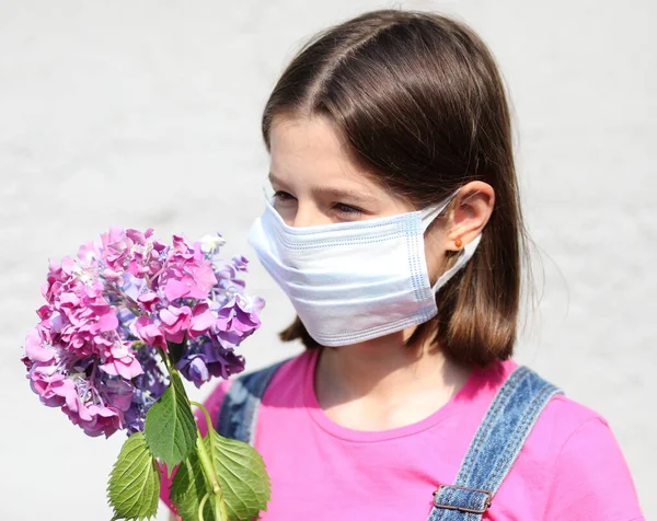 小さな女の子とともに外科用マスクのための保護コヴィト 19と持っていますアジサイの花 — ストック写真