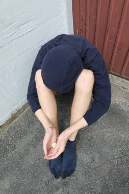 Kapüşonlu kazaklı genç evsiz adam şehrin bir köşesinde sadaka istiyor.