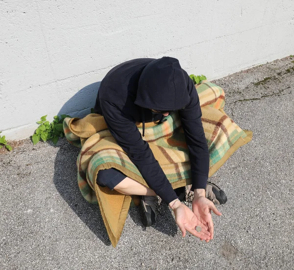 homeless man begging on the street under an old blanket