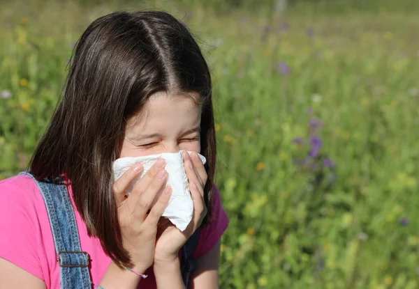 若い女の子はくしゃみをし花の畑で白いハンカチで鼻を吹く — ストック写真