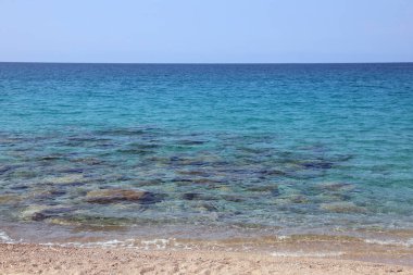 Yazın Akdeniz adasının taşlı kumlarıyla, insansız güzel, el değmemiş bir deniz.