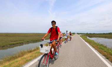 Aile yazın Venedik adası yakınlarındaki bisiklet yolunda bisiklet pedalları kullanıyor.