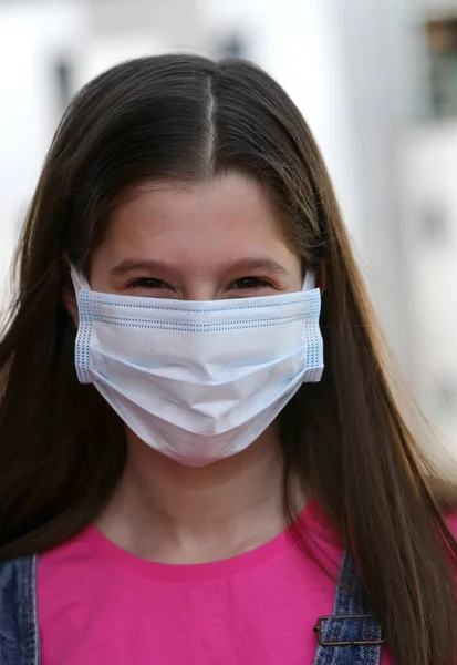 世界的な流行の中でコロナウイルスから身を守るために外科用マスクの後ろで笑顔で長い黒い髪をした若い女の子 — ストック写真