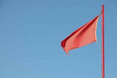Kırmızı bayrak mavi gökyüzünün arka planında tehlikeli bir durumu gösteriyor.
