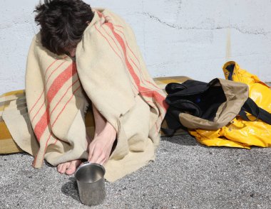 Genç evsiz bir adam bir şiltenin üzerinde oturuyor ve kirli bir battaniyenin altında...