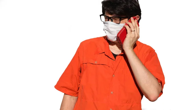 マスクとオレンジのシャツを着た男が白い背景で電話をかけながら — ストック写真
