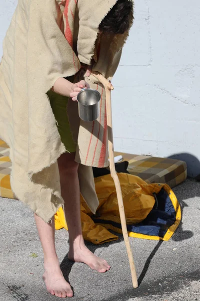 一个跛脚的流浪汉拿着手杖走在肮脏的毛毯上 向镇上的人要钱 — 图库照片