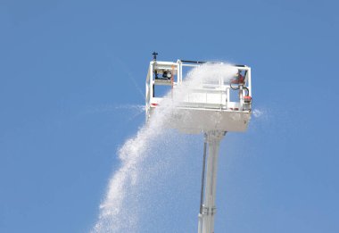 İtfaiye arabasının entegre yangın musluğuyla dolu sepeti su ve kendini söndüren köpük maddesiyle birlikte mavi gökyüzünden görüldü.