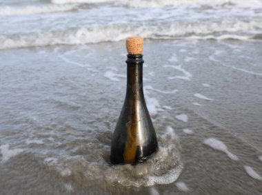 bottle with a message inside on the beach by the sea with waves