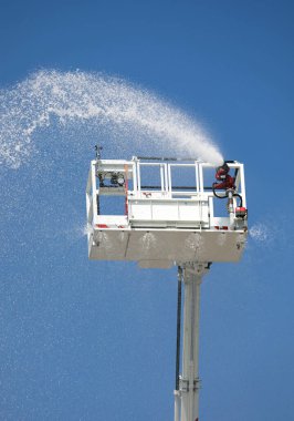 İtfaiye arabasının entegre yangın musluğuyla dolu sepeti su ve kendini söndüren köpük maddesiyle birlikte mavi gökyüzünden görüldü.