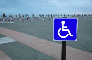 Tekerlekli sandalyedeki mavi tabela kumsaldan güvenli bir şekilde geçmek için uygun yolu gösteriyor.