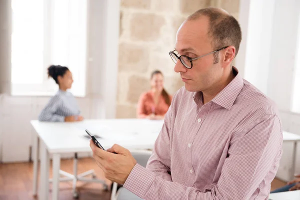 ピンクのシャツとメガネの白人男性は テキスト メッセージを送信する Office 設定に座ってください — ストック写真