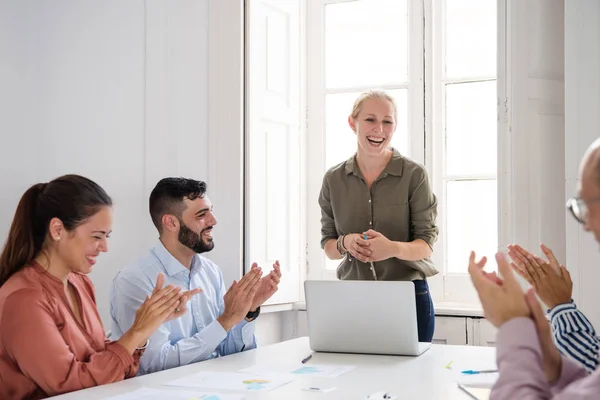 Successful group of office colleagues laughing and clapping motivated for the woman in a green shirt