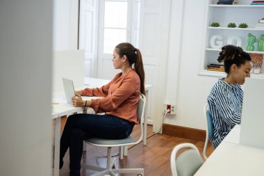 Bir açık plan ofis bilgisayarlarda çalışma sandalyelere oturan iki kadın