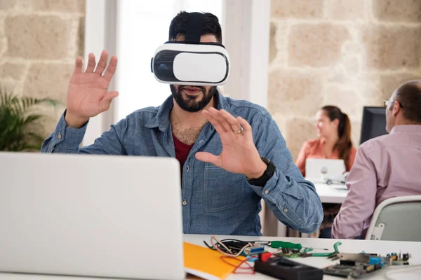 人在办公室坐在桌和测试虚拟现实玻璃作为同事会议在背景发生 — 图库照片
