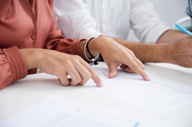 Beyaz gömlekli bir adam yanında oturur gibi masa başında oturan ve bir belgeyi işaret eden kadın o üzerinden okuyor