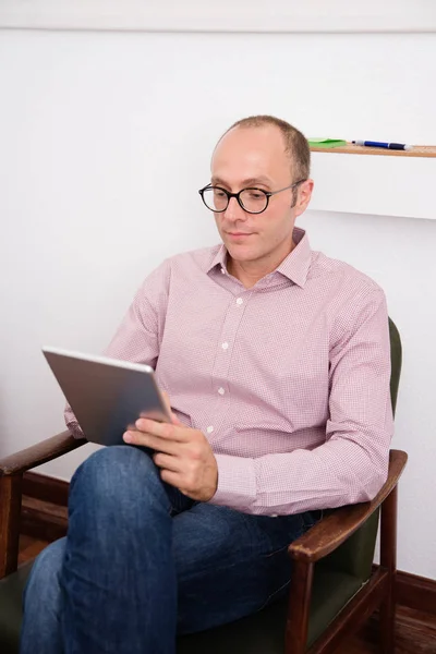 Mężczyzna Trzymając Tablet Jak Czyta Siedząc Krześle Nogami Skrzyżowanymi — Zdjęcie stockowe