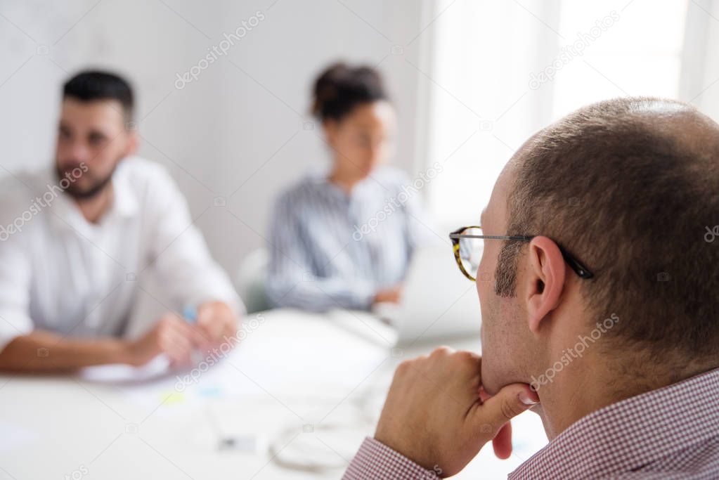 Business meeting held in a boardroom the man and woman are out of focus the man with glasses and pink shirt sits in the forefront