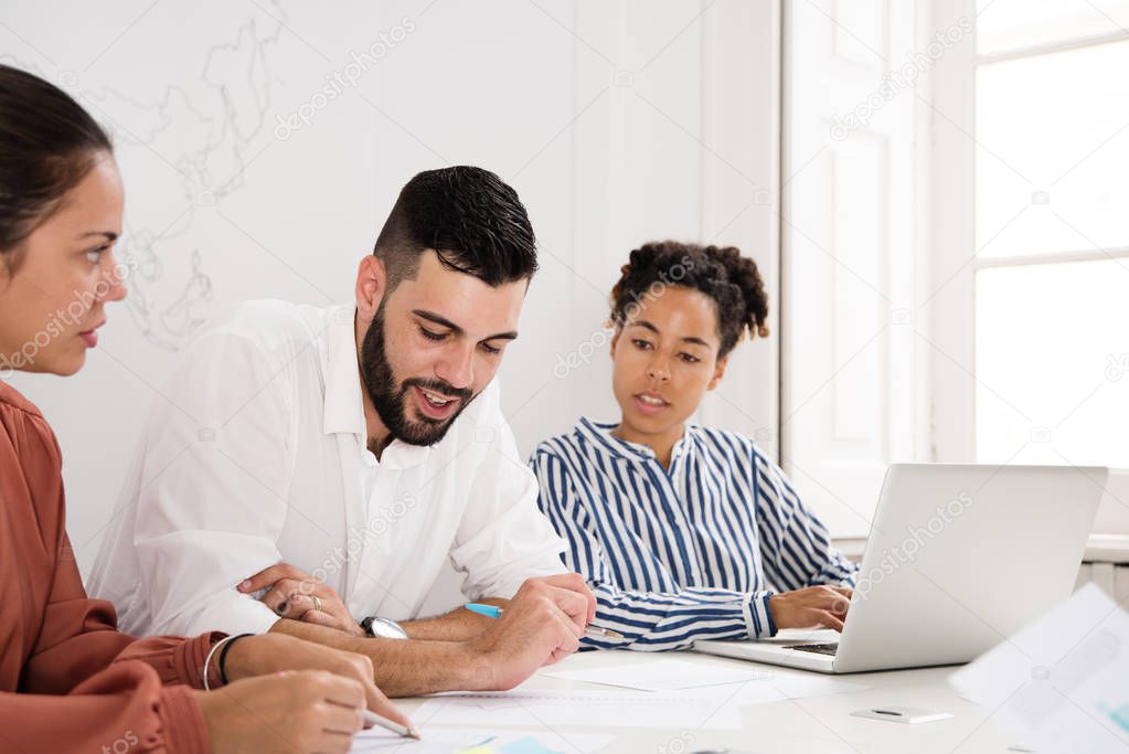Two women and a man sitting at a desk holding a meeting, the man is looking down a document