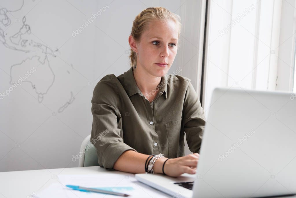 Young woman sitting behind a desk, typing on a laptop in an office