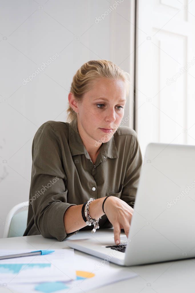 Seated woman working with laptop as she sitting at a desk in an office