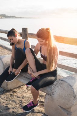 İki genç kadın tarafından deniz kıyısında bir bankta oturmuş, onlar onların ayakkabı bağcığı bağlama