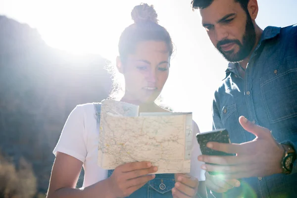 Woman is looking at a map, man standing next to her and holding a phone, they are both in the desert