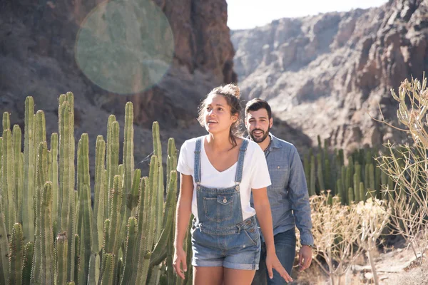Couple walking past cactus and bushes as they walk along a mountain path