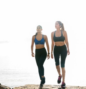 Okyanus parlak güneş ışığı altında plaj boyunca yürüyen iki kadın koşucu