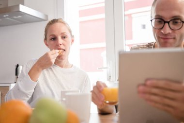 Bir masada oturan ve bir pc tablet vasıl arıyorsunuz bir çift. adam bir bardak portakal suyu tutar ve yiyor