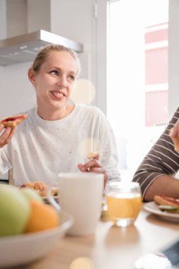 Bir masa ve yemek ve onun arkadaşı, gülümsüyor, oturan kadın beyaz duvarlar ve büyük pencereler ile mutfak bulunmaktadır