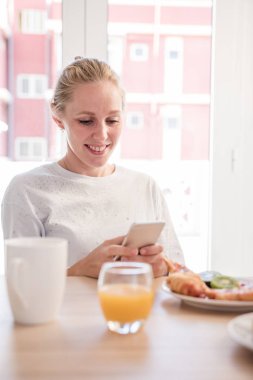 Kadın gülümseyerek ve aşağı bakıyor bir cep telefonu kahvaltı masasında