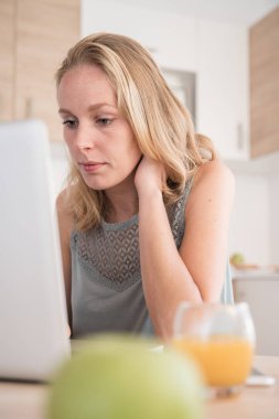 O evden çalışan bir dizüstü pc dikkatle bakar gibi ileri bir mutfak yaslanmış bir masada oturan kadın
