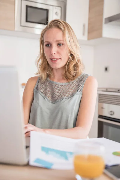 Mujer Sentada Una Mesa Una Cocina Mirando Una Computadora Portátil — Foto de Stock