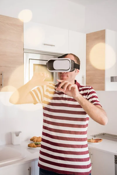 男人握住他的手对他的脸 因为他看通过虚拟现实的眼镜 因为他站在厨房里 — 图库照片