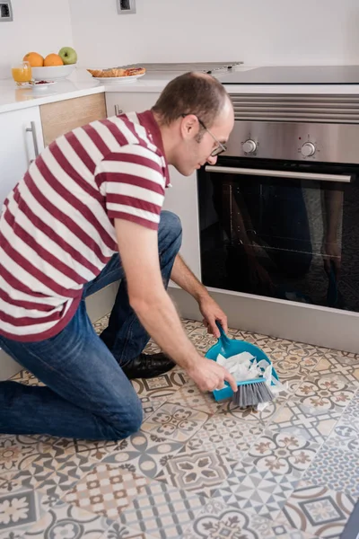 Man sweeping dirt into a dust pan on a kitchen floor