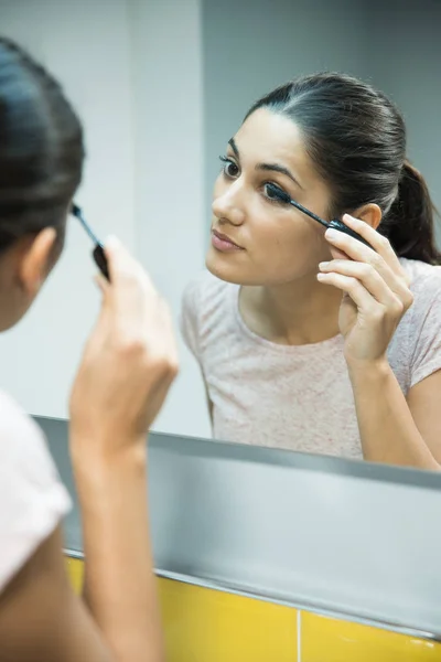 妇女靠在镜子附近 因为她涂睫毛膏她的睫毛 — 图库照片