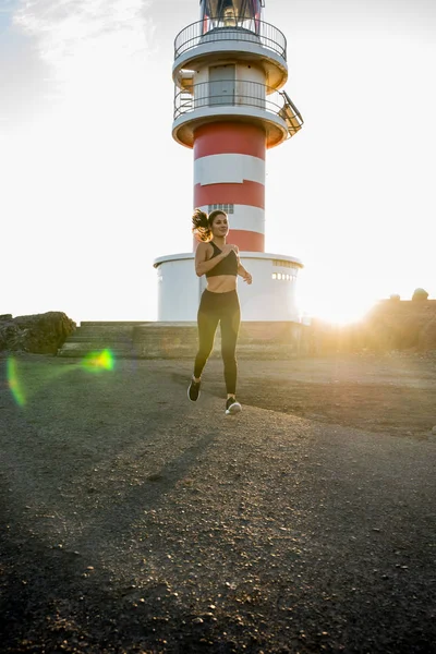 Woman running past a light as the sun rises in the distance in the sunset