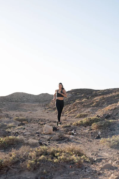 Long distance shot of a woman running down hill in the desert, along a rocky path