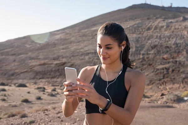 Žena Drží Mobil Sms Zatímco Ona Nosí Sluchátka Stojí Poušti — Stock fotografie