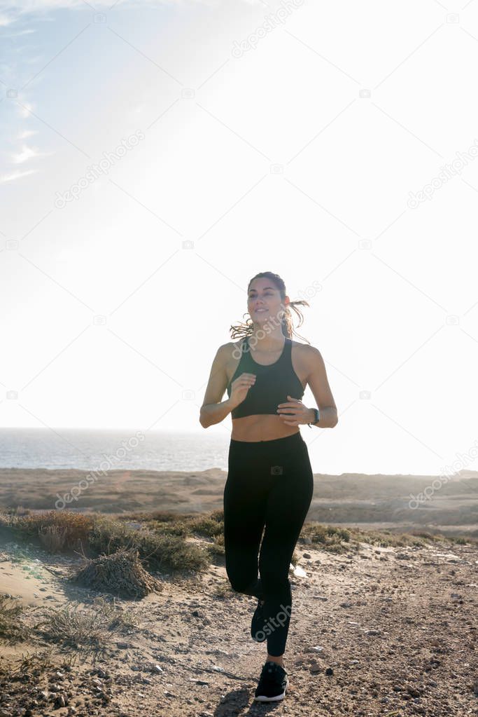 Jogging woman running in the desert as she runs along a brown and sandy raod
