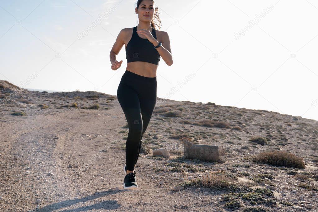 Woman sprinting as she runs on a sandy dark stone road, she is running downhill