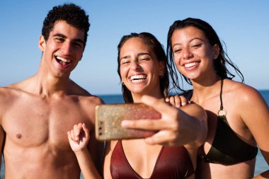 Bir grup genç elinde cep telefonu yla selfie çekerken kameraya gülüyor.