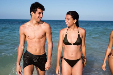 Genç adam ve kadın, okyanustan sahile doğru yürürken birbirleriyle konuşuyorlar.