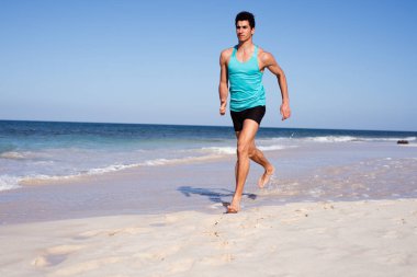 Young man running with his arms at his side on the beach in summer