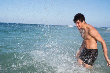 Okyanusta duran genç adam ve su toplamak için kollarını geri süpürür sıçrama