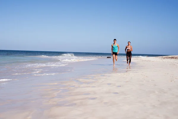 Young couple jogging in a long distance shot along a sandy white beach