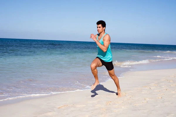 Young dark haired man dressed in running gear lift his leg as he takes a step while running on the beach