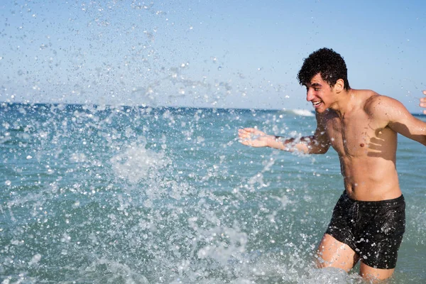 Young man stands with his hands apart as stand in the ocean splashing water
