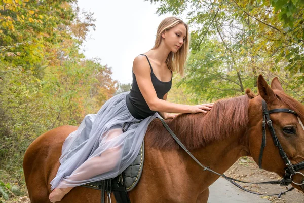Una joven rubia posando con un caballo, una hermosa chica y un caballo fuerte . — Foto de Stock
